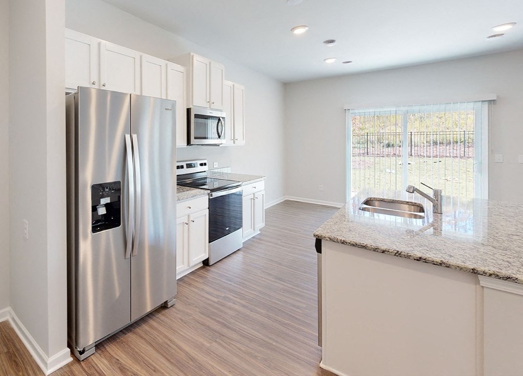 A kitchen with a refrigerator, microwave, oven, and sink.