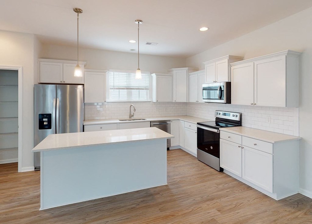 A modern kitchen with white cabinets and a wooden floor.