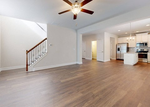 A spacious living room with a staircase and a kitchen in the background.