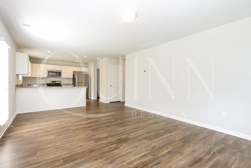 a spacious living room with hardwood floors and a kitchen in the background
