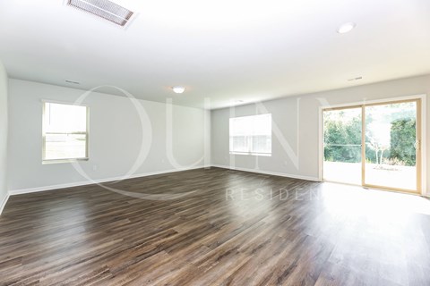 A spacious room with wooden flooring and large windows.
