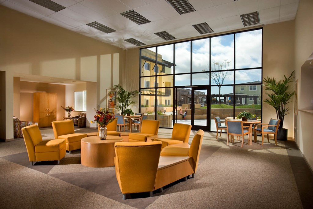 a lounge area with yellow chairs and tables and a large window