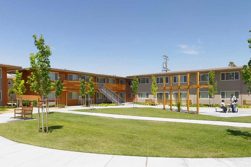 a courtyard with trees and a grassy area in front of a row of buildings