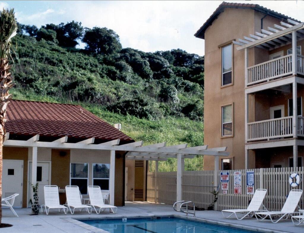 the pool and patio of a hotel with white chairs