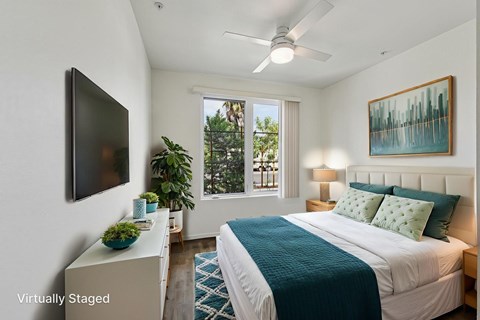 A bedroom with a bed, a television, a plant, and a painting on the wall.