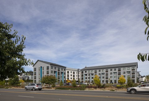A grey building with a blue stripe on the side is surrounded by trees and cars.