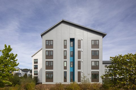 A modern building with a grey facade and a blue door stands in front of a cloudy sky.