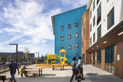 A playground area with a yellow slide is located outside a blue building.