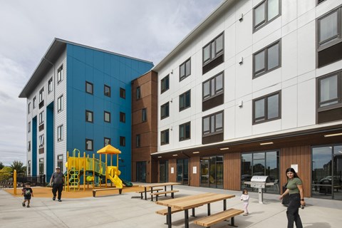 A playground area in front of a modern building with a blue and white building to the left and a white and brown building to the right.