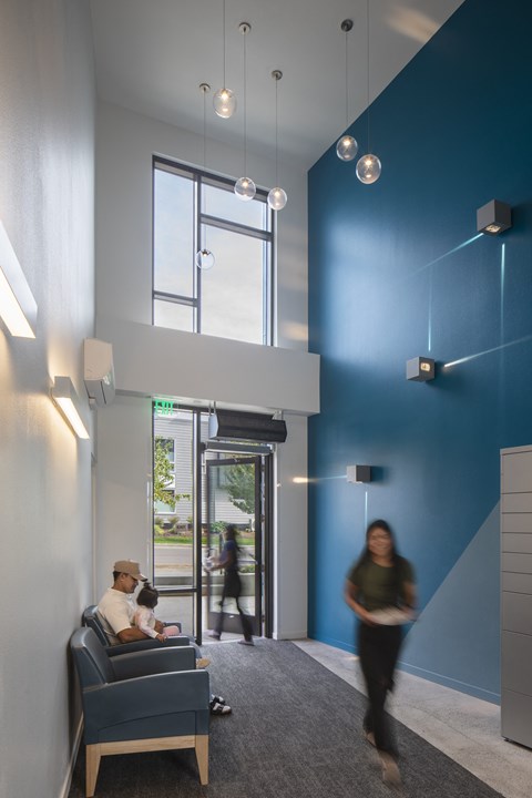 A man is sitting on a blue chair in a room with a large window.
