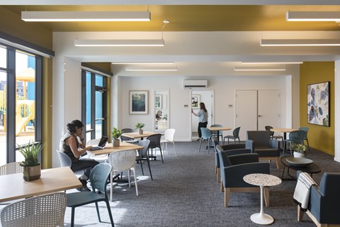 A woman is sitting at a table in a brightly lit room with yellow walls.