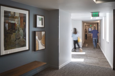 A hallway with a green exit sign and people walking.