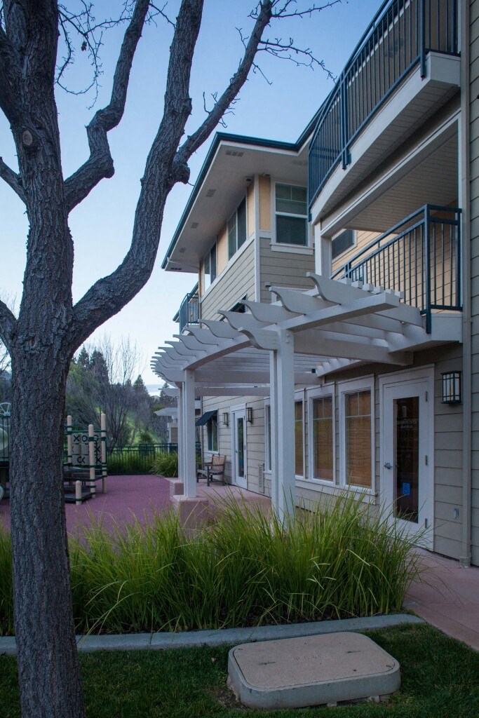 the outside of an apartment building with a porch and a tree