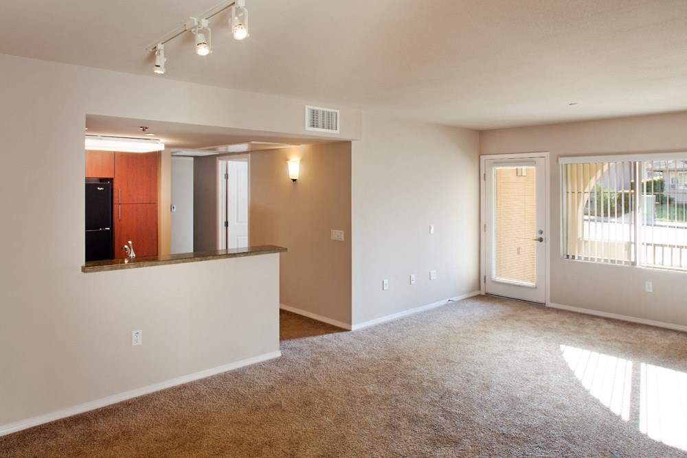 an empty living room with a kitchen and a glass door