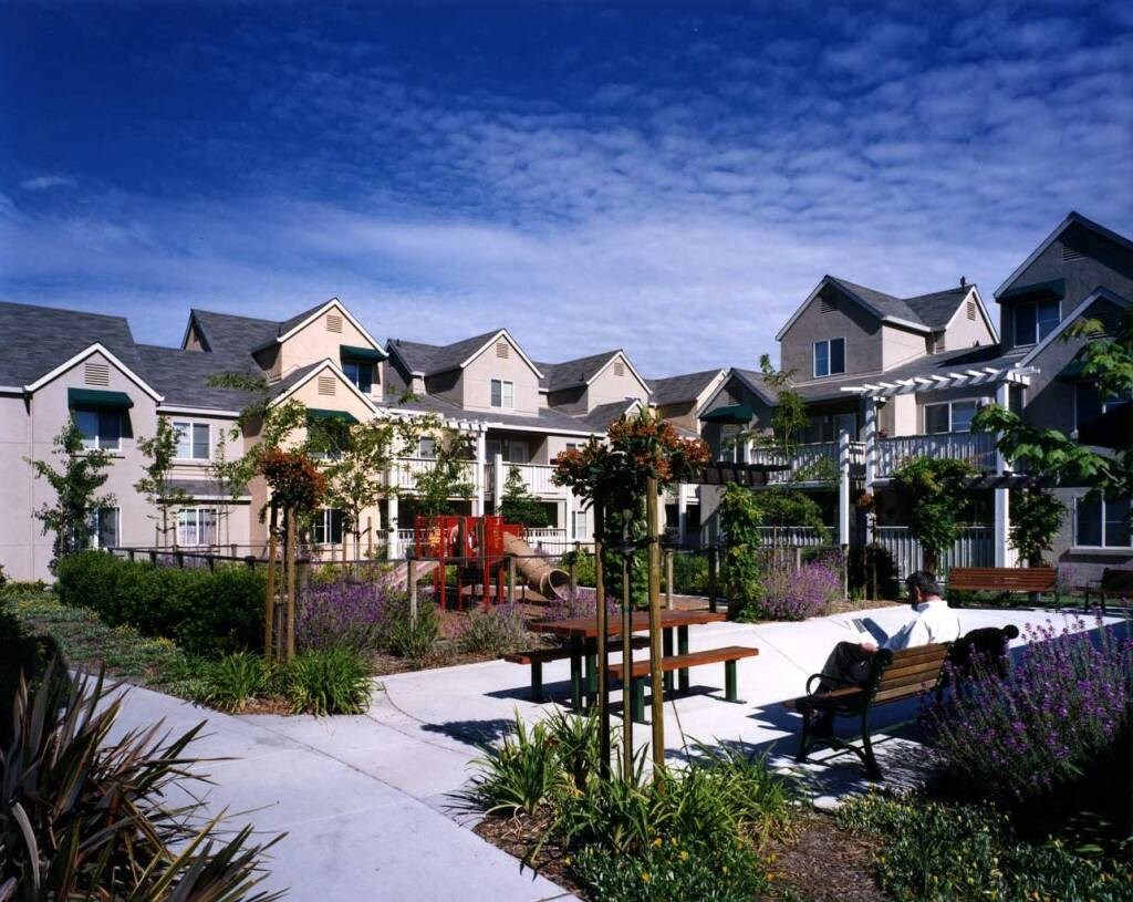 a man sitting on a bench in a garden in front of houses