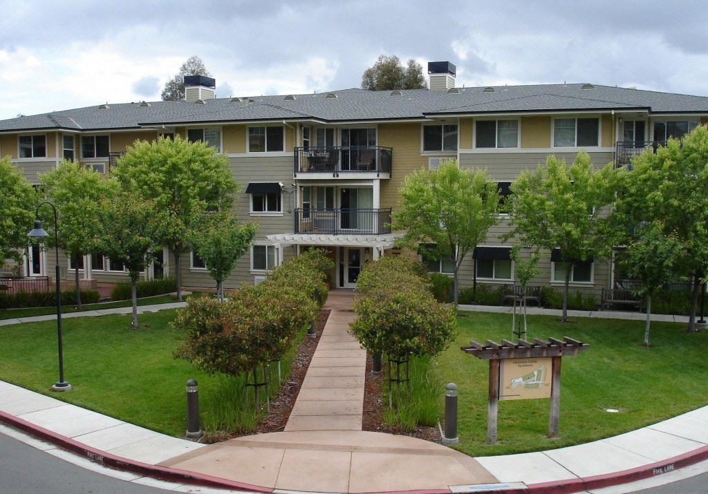 an exterior view of an apartment building with a green lawn and trees