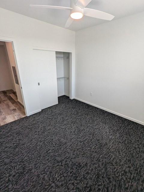 A room with a carpeted floor and a ceiling fan.