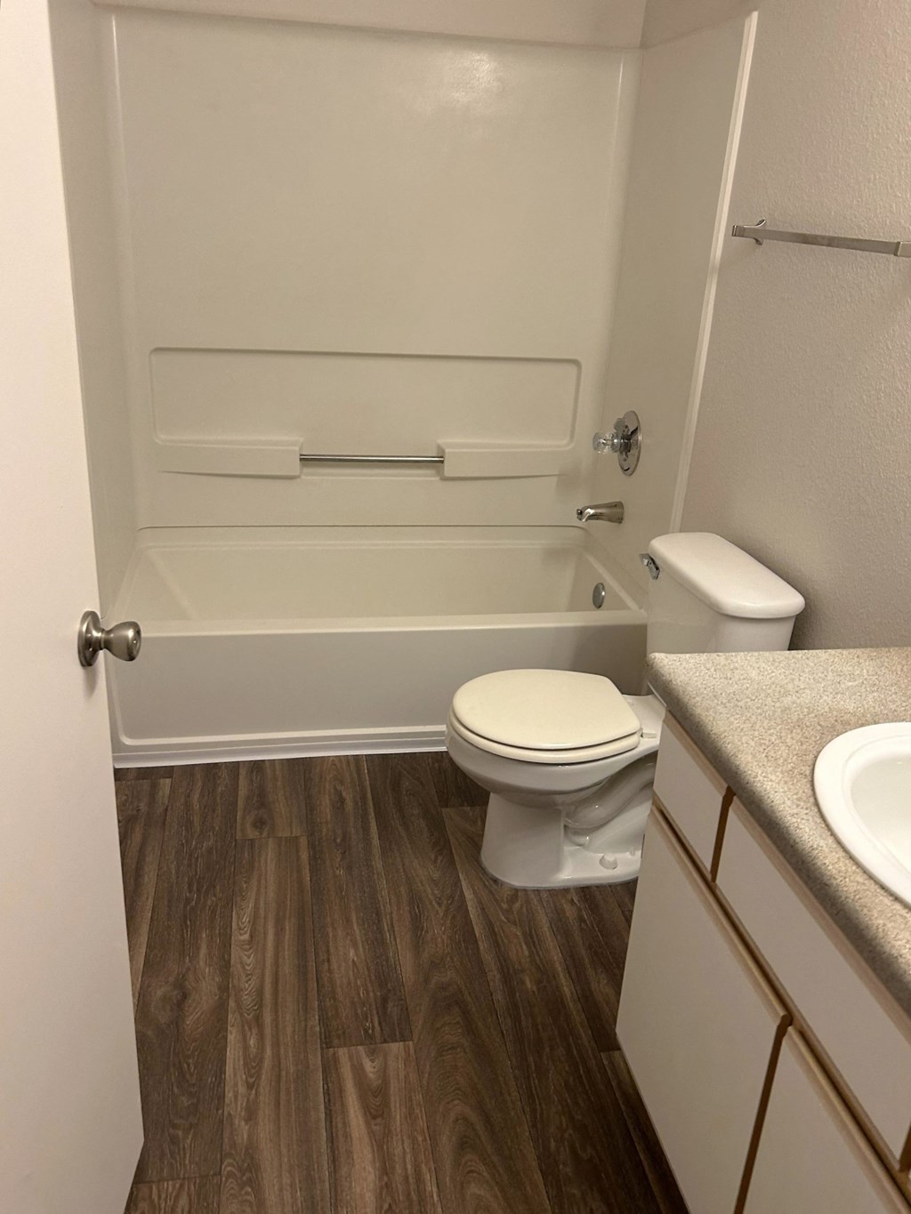 A white toilet sits in a bathroom with wood flooring and a white sink.