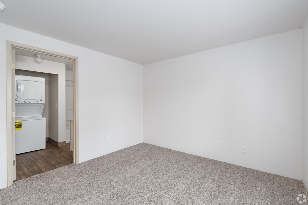 A white room with a doorway leading to another room with a fridge.