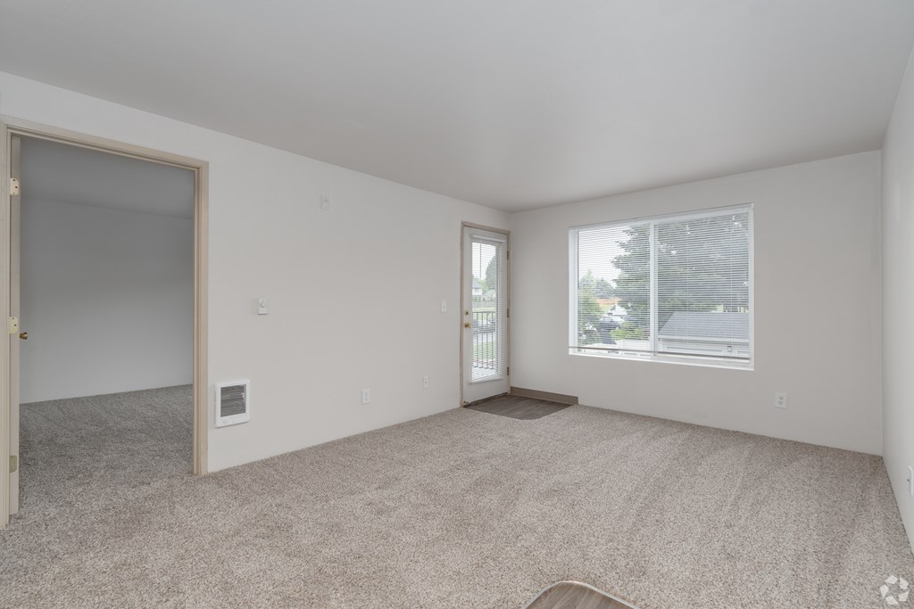 A spacious empty room with carpeted floor and two windows.