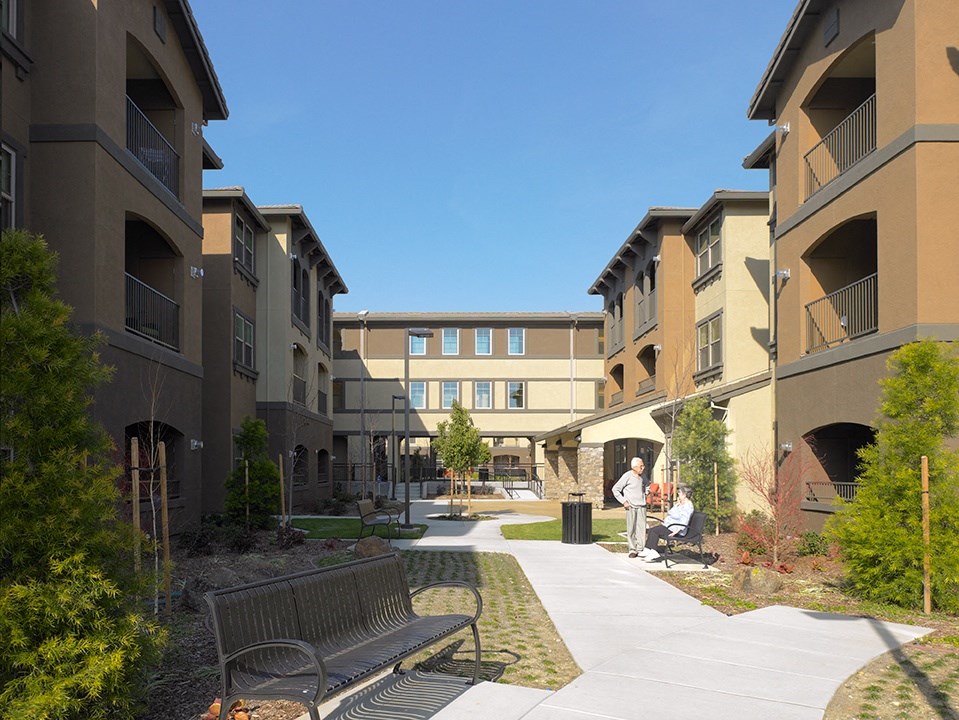 a pathway between two apartment buildings with benches and trees