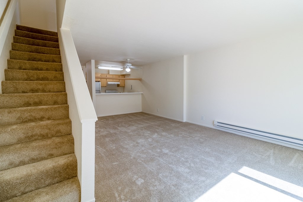 an empty living room with stairs and a kitchen