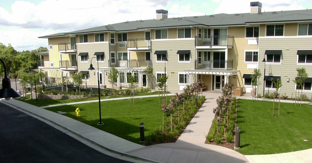 an apartment building with green grass and a sidewalk in front of it