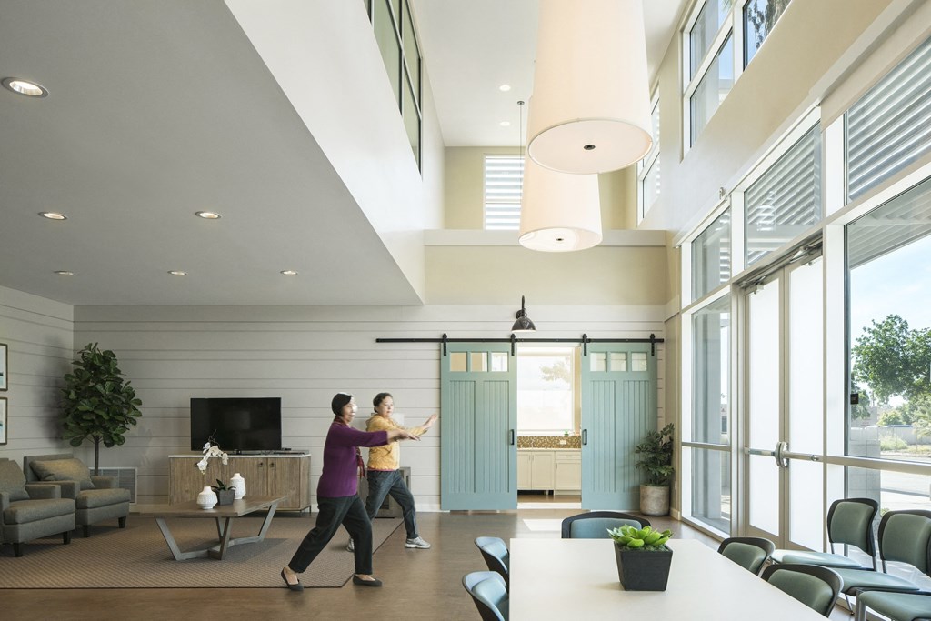 two people walking through a living room with large windows