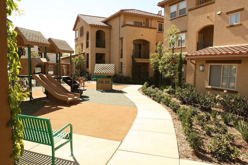 a courtyard with a playground and benches in an apartment complex