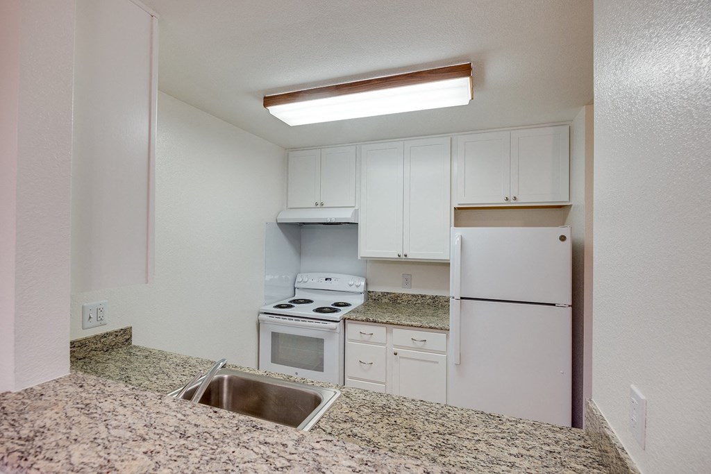 an empty kitchen with white appliances and granite counter tops