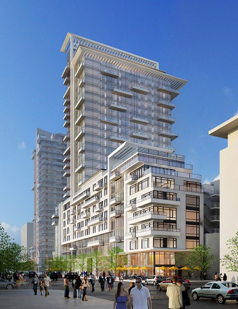 A modern multi-story building with balconies and large windows is surrounded by a crowd of people.