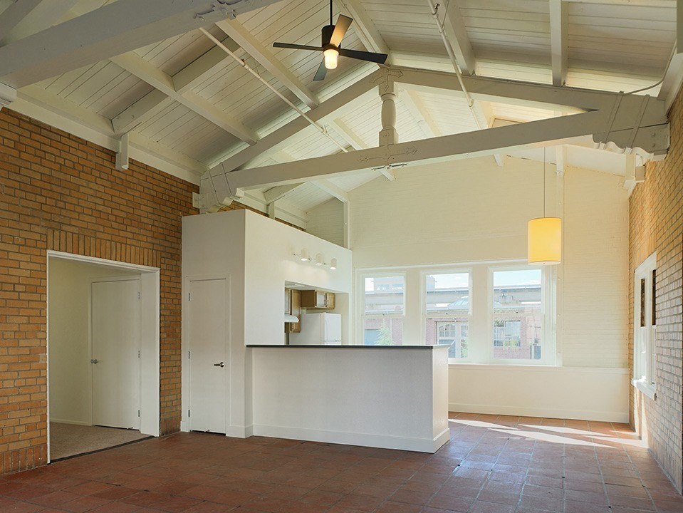 an empty living room with a kitchen and a ceiling fan
