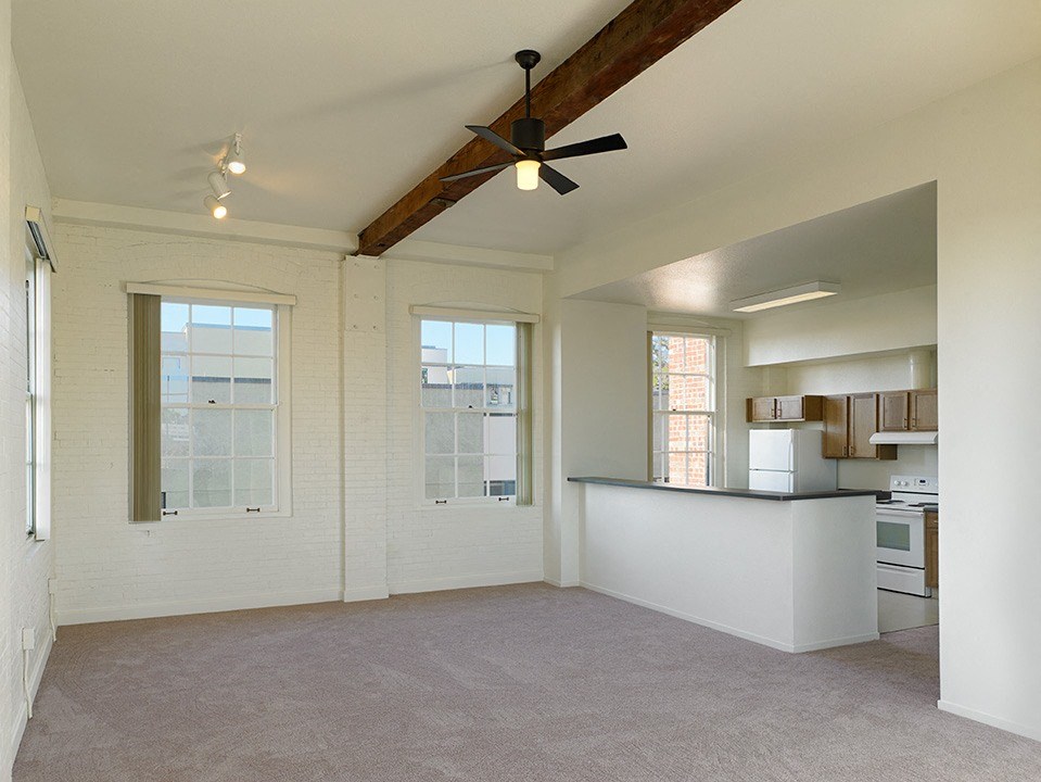 an empty living room with a ceiling fan and a kitchen