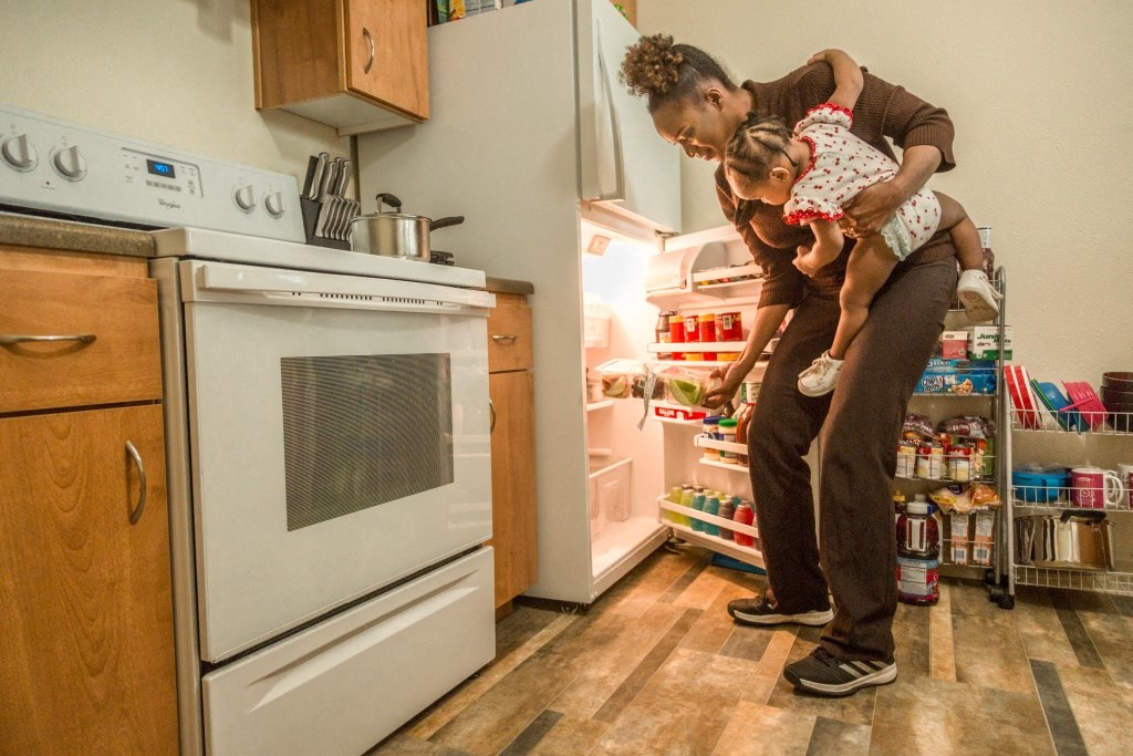 a woman holding a child in a kitchen with an open refrigerator