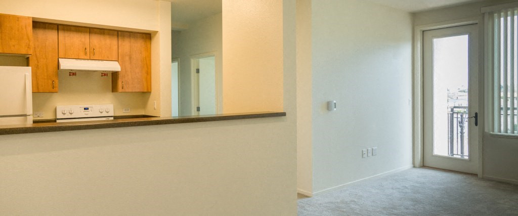 an empty living room with a kitchen and a glass door