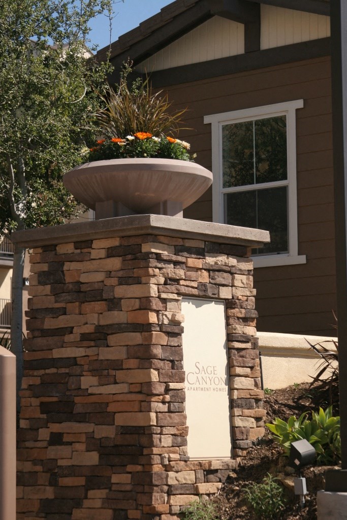 a stone pillar with a potted plant on top and a sign on the side