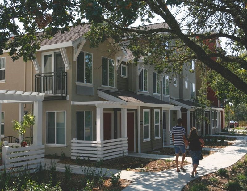 a man and woman walking down a sidewalk in front of an apartment building