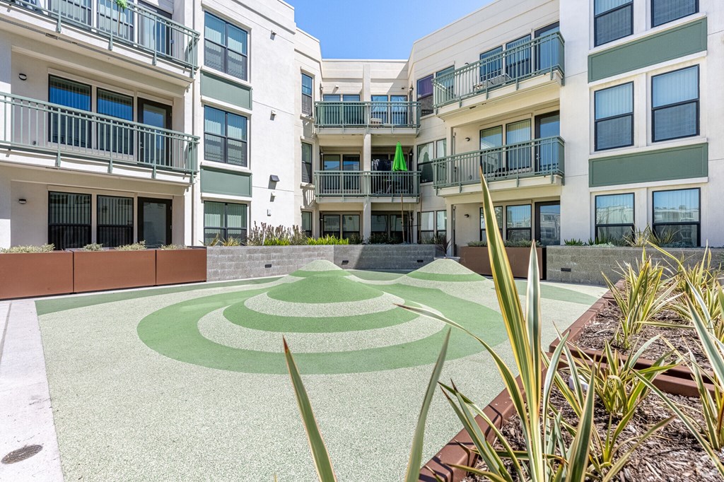 A courtyard with a green and white patterned ground and a building with balconies in the background.