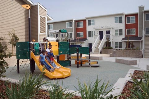 two children playing on a playground in front of apartments