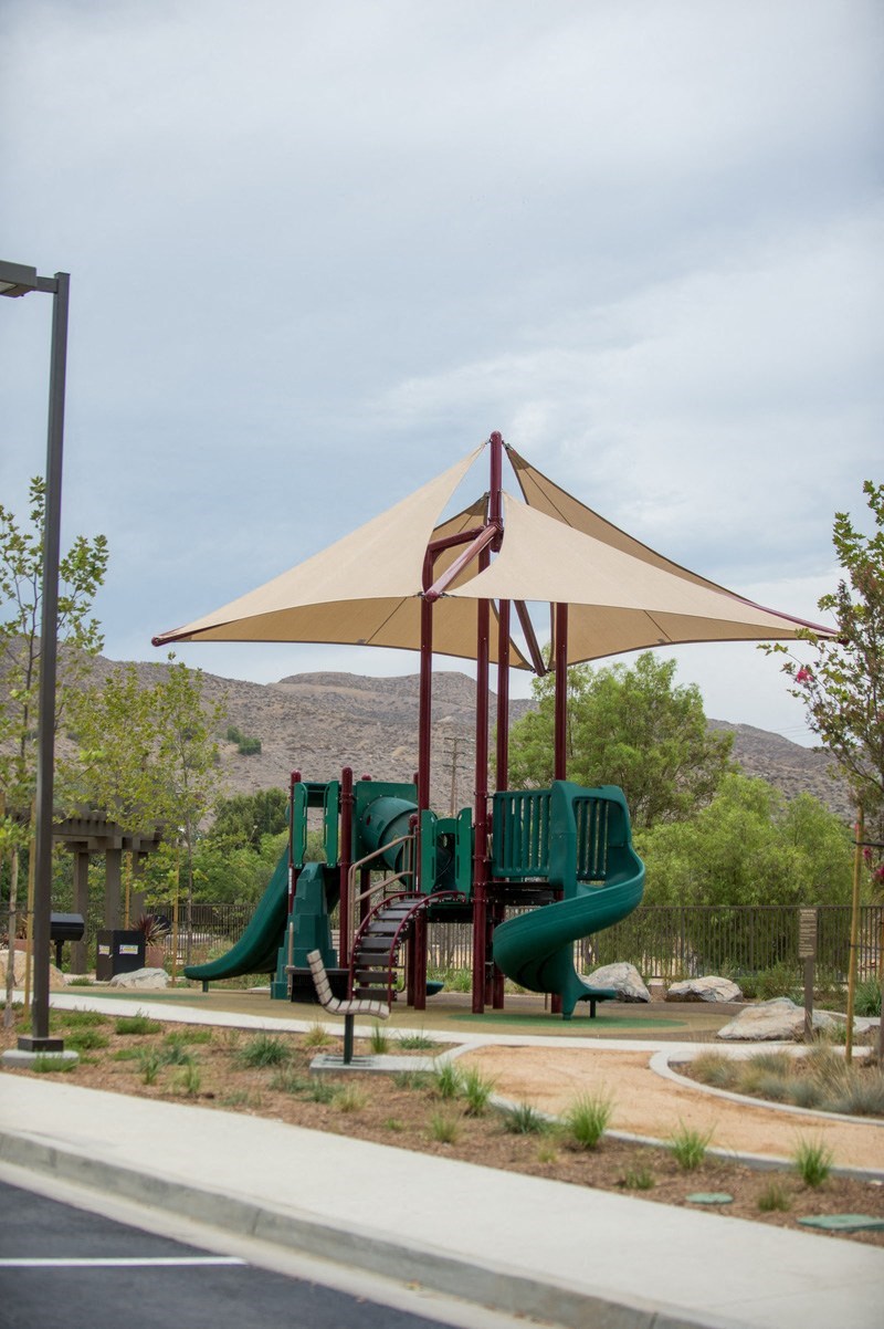 a playground with green slides and a tan umbrella