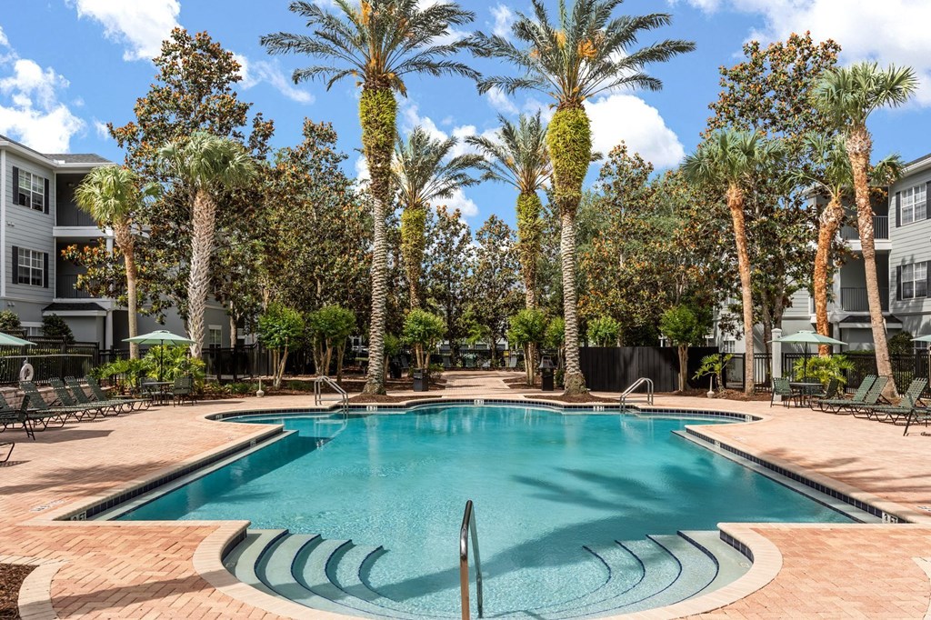 A swimming pool surrounded by palm trees and a building in the background.
