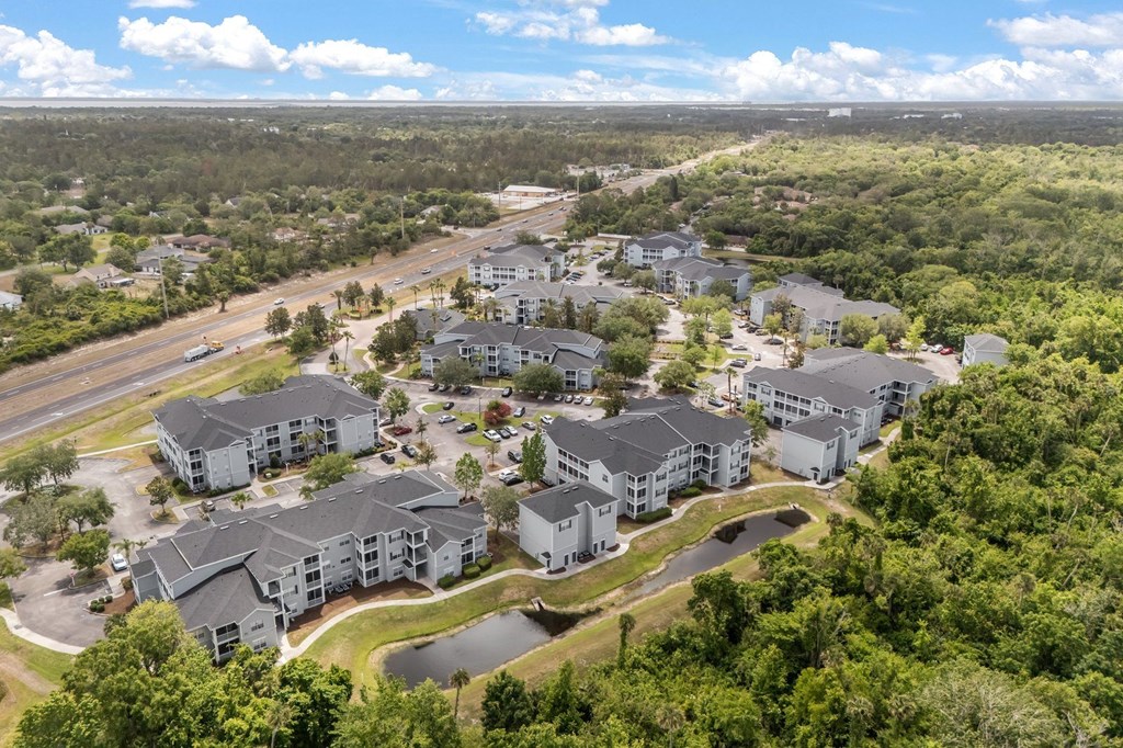 A bird's eye view of a residential complex surrounded by greenery and a highway.