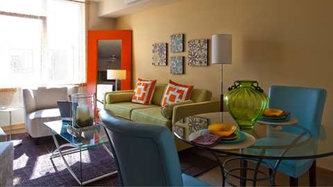 A living room with a glass table and a green vase on it.