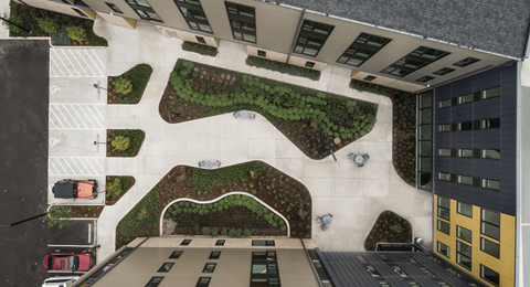 A parking lot is surrounded by a building and a green space.