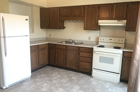 A white refrigerator stands in a kitchen with wooden cabinets and a white stove.