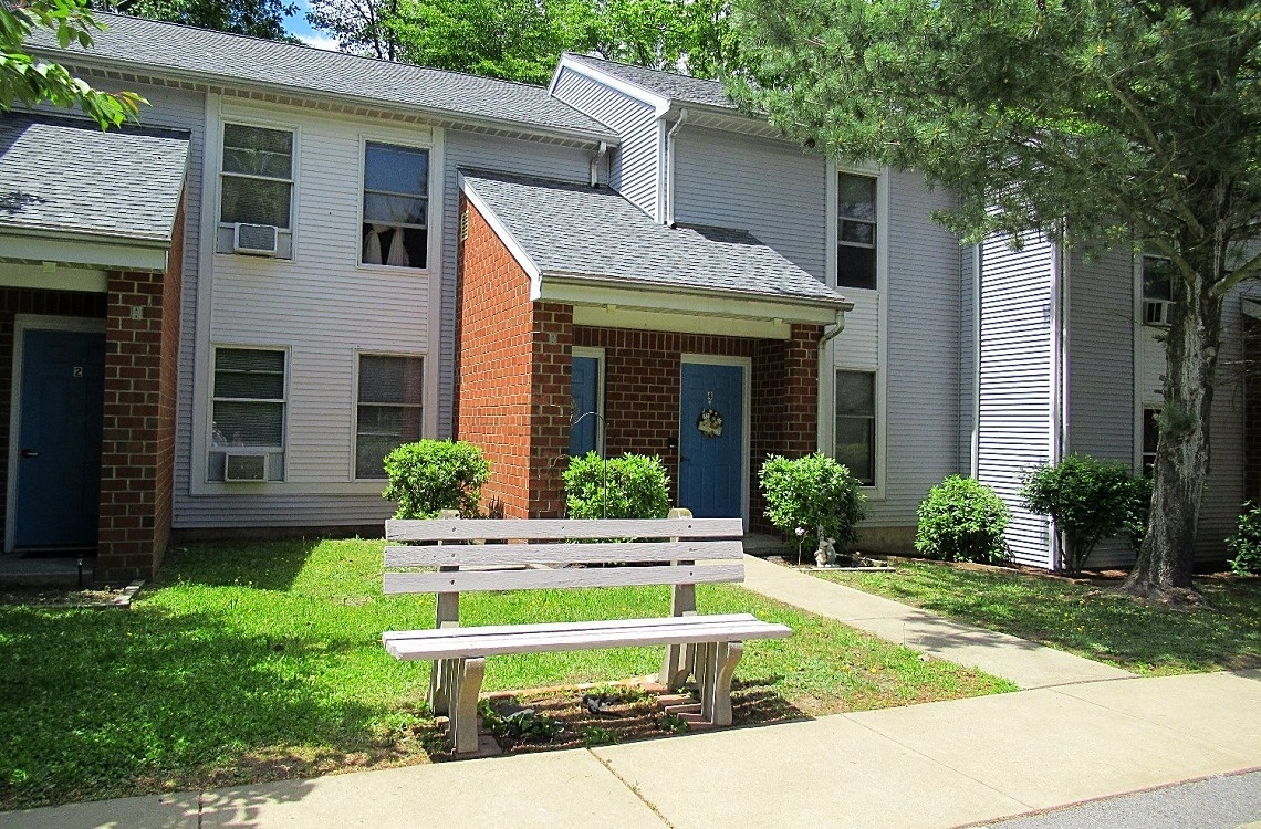 A bench sits in front of a brick building with a blue door.