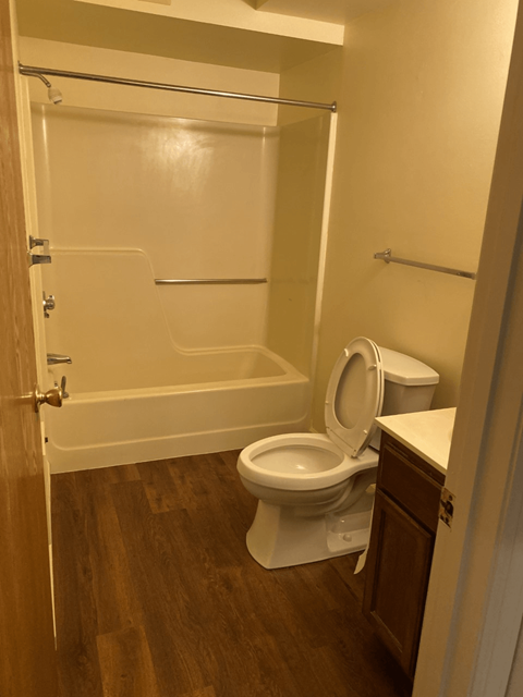 A white toilet in a small bathroom with wood flooring.