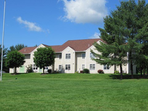 A white building with a brown roof is surrounded by a green lawn.