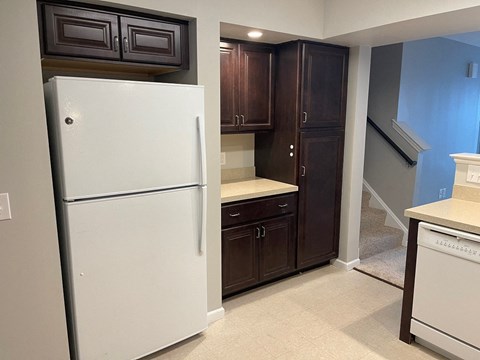 A white refrigerator stands in a kitchen with dark brown cabinets.