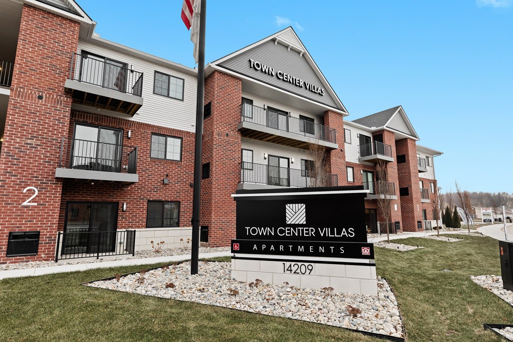 A sign for Town Center Villas Apartments stands in front of a brick building.